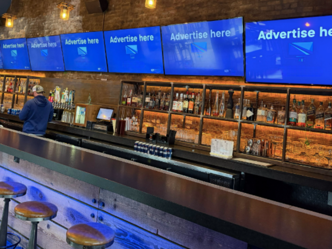 Venue advertising displayed on multiple screens inside a bar or restaurant